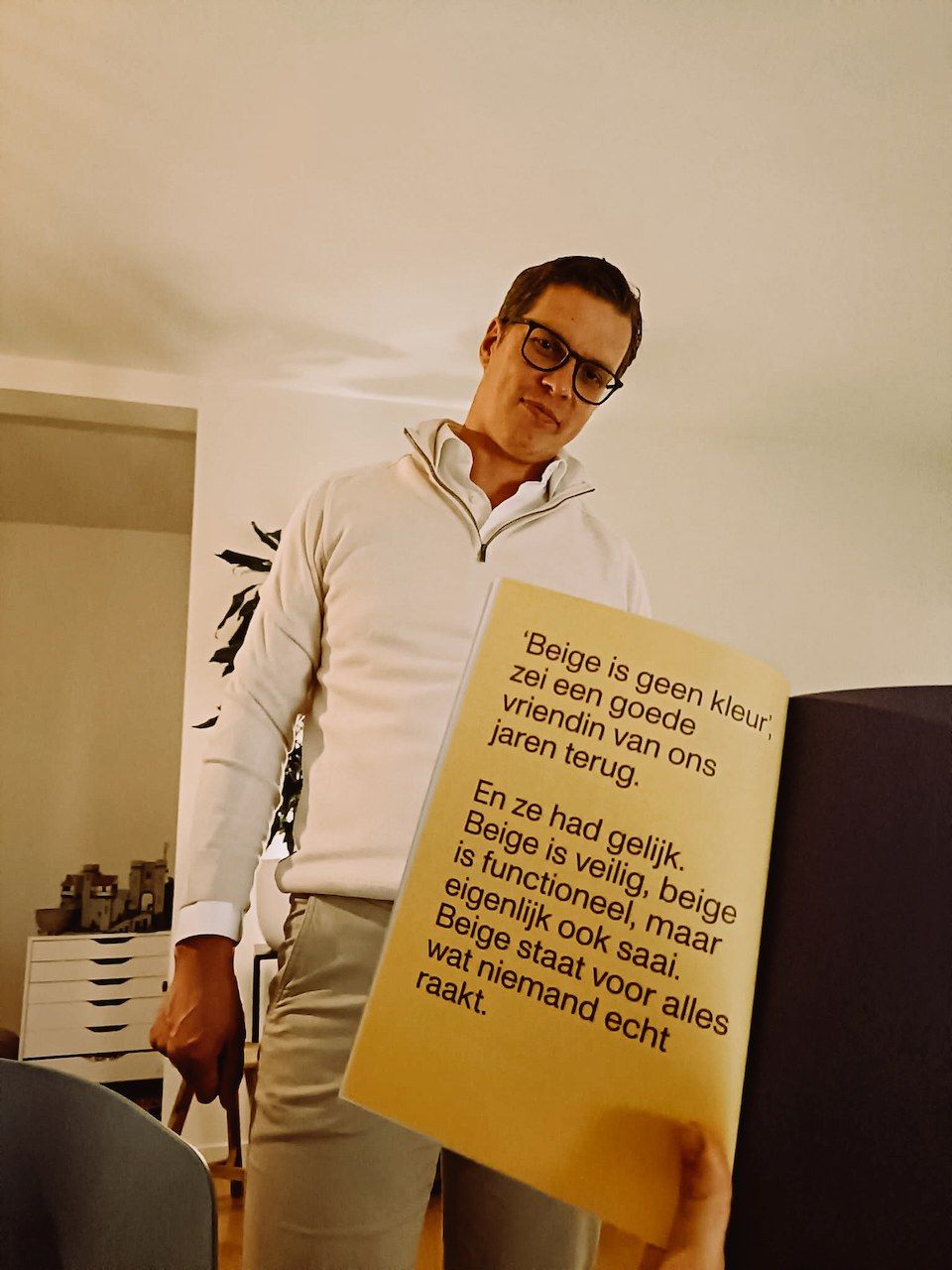 Polle in a beige jumper and trousers, holding the book open at the page that says beige is not a colour