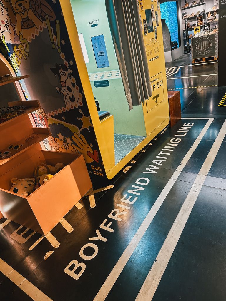 A store floor with the words Boyfriend waiting line painted in white next to a yellow photo booth