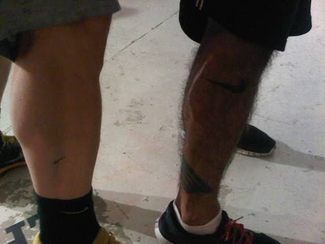 Two runners seen from behind, one with a Nike swoosh tattooed on his calf