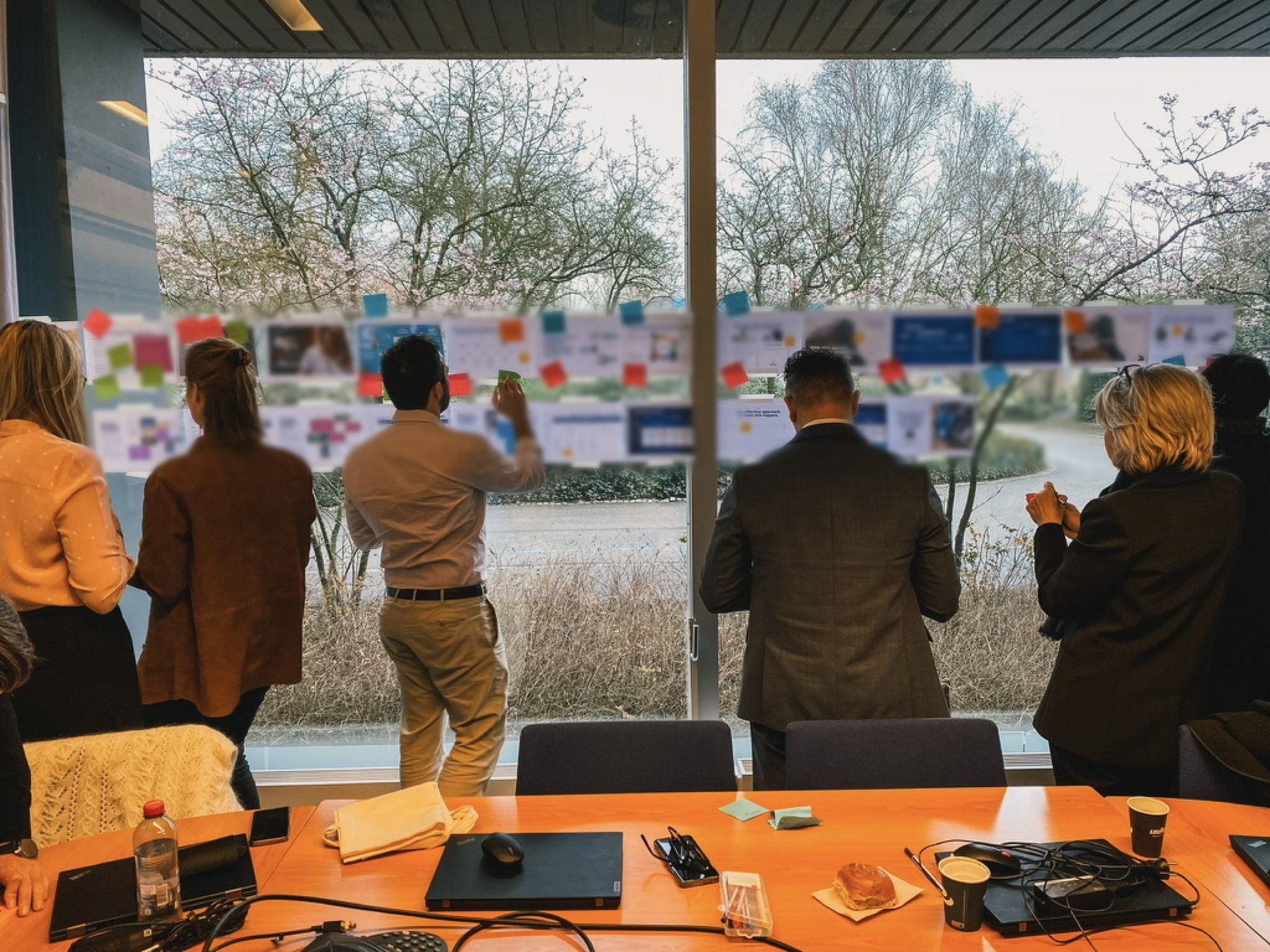 A team at a window full of printed slides and sticky notes, seen from behind
