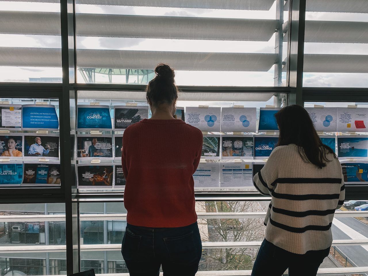 Two people reading a storyline taped to a window, seen from behind