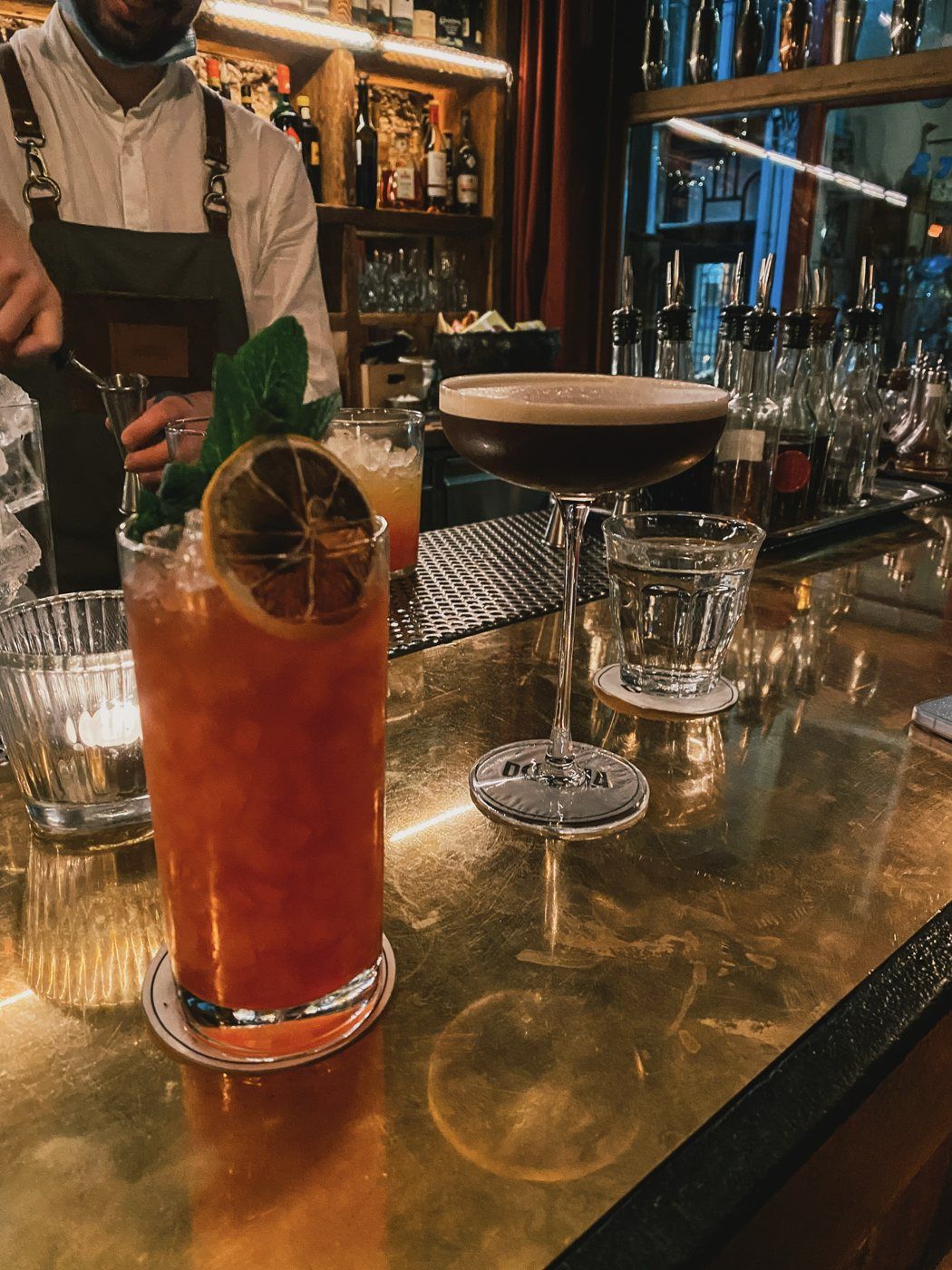 Cocktails on a brass bar in Antwerp, a bartender at work behind them